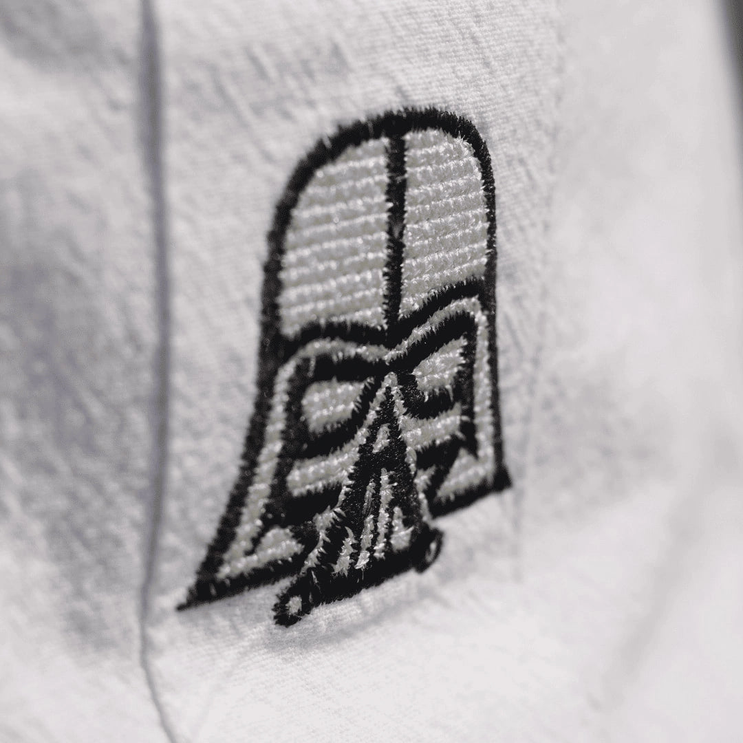 Detalle del bordado que representa al icónico líder del lado oscuro con su casco negro, resaltando la precisión de la costura y el diseño minimalista en contraste con el blanco.