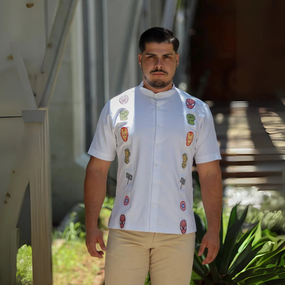 Modelo masculino posando con una guayabera blanca de manga corta en lino y algodón, destacando bordados de símbolos de unión y fuerza inspirados en un universo de héroes legendarios, de Guayaberas LeMaan.