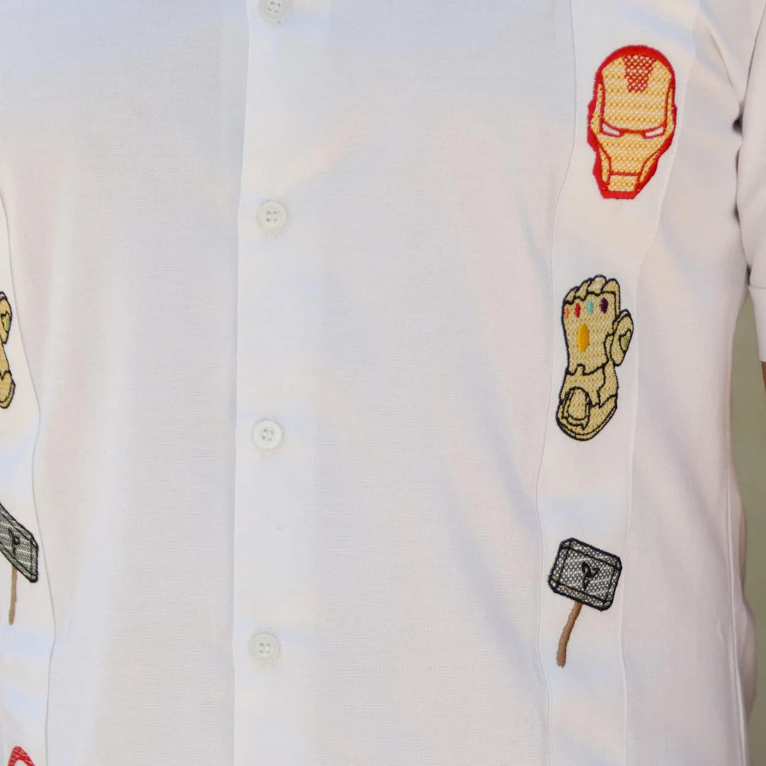 Acercamiento al bordado artesanal de figuras estilizadas y emblemas de valentía sobre tela blanca de lino premium, resaltando la textura y la precisión de los acabados de alta costura.